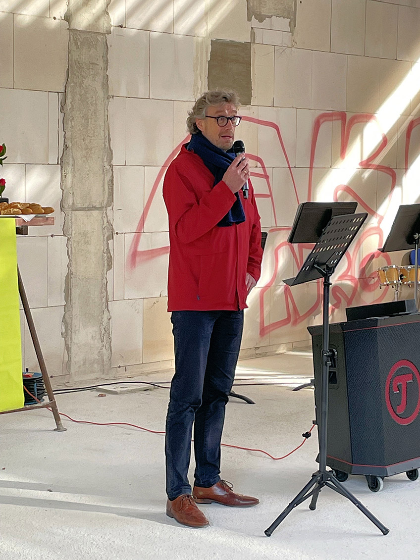 Hoch hinauf musste B&uuml;rgermeister Michael J&auml;cke, um zu pr&uuml;fen, ob der Richtkranz am Rohbau der Sporthalle des Ratsgymnasiums auch richtig h&auml;ngt. Vom rund 8,50 Meter hohen Ger&uuml;st reichte er dem Zimmermann den obligatorischen Schnaps zum Richtspruch. Dieses Ritual verfolgten bei bestem Wetter am 11. November rund 60 G&auml;ste, die die Schule und die Stadt als Bauherrin zum Richtfest eingeladen hatten. Den Auftakt machte in der k&uuml;nftigen Sporthalle die Bigband des Ratsgymnasiums mit dem St&uuml;ck &bdquo;Eye oft he Tiger&ldquo;. Nach den Gru&szlig;worten gaben die Sch&uuml;ler*innen dann noch &bdquo;We are the Champions&ldquo; zum Besten.     &bdquo;Movimens&ldquo; - das ist der Name, den das Ratsgymnasium dem Neubau geben will, wenn er in den Betrieb geht, berichtete Schulleiterin Cordula K&uuml;ppers am vergangenen Freitag. Die Halle befinde sich &bdquo;mitten im Kiez&ldquo; der Altstadt und solle k&uuml;nftig eine offene Sporthalle f&uuml;r das gesamte Quartier werden. Sie w&uuml;nscht sich auch, dass auf dem Kunstrasenplatz, der nach der Inbetriebnahme der Halle erneuert werden muss, wieder viel Fu&szlig;ball gespielt wird. Neben dem Schulsport k&ouml;nne es Angebote wie zum Beispiel Yoga-Kurse geben. Schon vor dem Bau gab es Kooperationen mit der Juxbude, der Volkshochschule, der Eine-Welt-Schule sowie mit anderen Nachbarn, so K&uuml;ppers.  Auf die im August 2021 abgerissene alte Einfach-Sporthalle sollte nicht ein gleich gro&szlig;er Ersatzbau aufgesetzt werden, erl&auml;utert Stadtk&auml;mmerer Norbert Kresse, der auch f&uuml;r die Geb&auml;udewirtschaft verantwortlich ist. Angedockt an die Halle werde es &ndash; nach einem l&auml;ngeren, gemeinsamen Planungsprozess zwischen Stadt und Schule - k&uuml;nftig einen Raum f&uuml;r sporterg&auml;nzende Nutzung wie zum Beispiel Tanzen/Gymnastik/Yoga und f&uuml;r den Sportunterricht auch einen Seminarraum mit Bild- und Filmpr&auml;sentation f&uuml;r den Bereich der Bewegungsanalyse geben. Dieser Raum k&ouml;nne auch von der VHS f&uuml;r beispielsweise Sprachkurse genutzt werden.   Die h&ouml;herwertige Ausstattung der Halle wurde &uuml;ber gesammelte Spenden des F&ouml;rdervereins finanziert. Zahlreiche Mindener Unternehmen und auch Stiftungen h&auml;tten das Projekt gro&szlig;z&uuml;gig unterst&uuml;tzt, wie die Vorsitzende der Gesellschaft der F&ouml;rderer des Ratsgymnasiums e.V., Verena B&ouml;cker, beim Richtfest stolz berichtete.  Der Neubau sei notwendig geworden, weil das Vorg&auml;nger-Modell &bdquo;in die Jahre&ldquo; gekommen war. Die Fassade hatte Risse, was zu einem gro&szlig;en Problem f&uuml;hrte, so B&uuml;rgermeister Michael J&auml;cke in seinem Gru&szlig;wort. Vor dem Hintergrund der vor allem krisenbedingten Mehrkosten bekr&auml;ftigte J&auml;cke vor den G&auml;sten die Entscheidung der Stadt, diese Halle zu bauen. &bdquo;Es ist richtig, dass wir das Projekt auch in schwierigen Zeiten angegangen sind und weiter vorangetrieben haben&ldquo;, so der B&uuml;rgermeister weiter.    Die Arbeiten liegen coronabedingt und aufgrund des andauernden Krieges in der Ukraine, der zu Materialengp&auml;ssen gef&uuml;hrt hat, nicht mehr im Zeitplan. Ferner musste das Baufeld durch den Kampfmittelr&auml;umdienst aufwendig sondiert und untersucht werden. Die deutschlandweit auftretenden Kostenexplosionen am Bau hat auch dieses Projekt - &uuml;ber alle Gewerke hin - hart getroffen: Waren die Planer anfangs noch von Projektkosten in H&ouml;he von 2,6 Millionen Euro ausgegangen, rechnet der Bereichsleiter der st&auml;dtischen Geb&auml;udewirtschaft, J&ouml;rn Schunk, aktuell mit 4,6 Millionen Euro - trotz unver&auml;nderter Planung. Der F&ouml;rderverein der Schule unterst&uuml;tzt den Neubau mit 150.000 Euro.    Bis Ende 2023 soll an der Ecke Rodenbecker Stra&szlig;e/Schwichowwall eine neue Einfachsporthalle mit 1.135 Quadratmetern Nutzfl&auml;che sowie dem angeschlossenen Raum f&uuml;r eine sporterg&auml;nzende Nutzung und den Seminarraum entstehen. Obendrauf kommen ein Gr&uuml;ndach und eine Photovoltaikanlage. Klimafreundlich sind auch die Energiequellen. Geheizt wird die Halle k&uuml;nftig mit einer Luft-Wasser-W&auml;rmepumpe plus Fernw&auml;rme und Solarzellen. &bdquo;Das sei zwar nicht die kosteng&uuml;nstigste Variante, aber &ouml;kologisch und zukunftsweisend&ldquo;, betonte B&uuml;rgermeister J&auml;cke.  Auch architektonisch galt es Herausforderungen zu meistern. So wird die Halle sehr gro&szlig;e Fenster zum Rasenplatz hin haben, um viel nat&uuml;rliches Licht in die Halle zu lassen. Die Fenster korrespondierten zun&auml;chst nicht mit den geforderten Sicherheitsstandards in Sporthallen. Aber auch daf&uuml;r wurde eine L&ouml;sung in Form einer zweiten Glaswand als Prallschutz von den Fachleuten der Geb&auml;udewirtschaft gefunden, so Schulleiterin Cordula K&uuml;ppers. Die Nutzer*innen k&ouml;nnen die Halle &uuml;ber zwei Eing&auml;nge erreichen &ndash; vom S&uuml;den und vom Norden her. Fahrradabstellpl&auml;tze sind im Nordwesten geplant.  Bis die neue Halle fertig ist, m&uuml;ssen die Sportlehrer*innen am Ratsgymnasium weiter kreativ sein. So w&uuml;rden andere Hallen in anderen Stadtbezirken genutzt. &bdquo;Wir fahren jetzt viel Bus&ldquo;, so K&uuml;ppers. Aber es gebe auch Sportunterricht drau&szlig;en, Tischtennis in der Aula und weitere Bewegungs-Ideen. Es lohne sich unbedingt auf die Halle zu warten, meint Cordula K&uuml;ppers. Ihr Dank und auch der des B&uuml;rgermeisters sowie der F&ouml;rdervereinsvorsitzenden galt den Mitarbeitern der st&auml;dtischen Geb&auml;udewirtschaft f&uuml;r die Planungen, Durchf&uuml;hrung und die Projektleitung sowie den &bdquo;flei&szlig;ig arbeitenden&ldquo; Handwerkern.